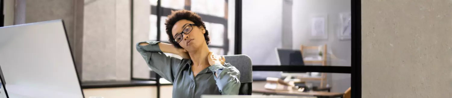 Woman experiencing neck pain while working at a computer, a common symptom of cervical disc problems.