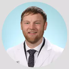 Photo of physician assistant Ace Camfield on a teal background in a white coat.